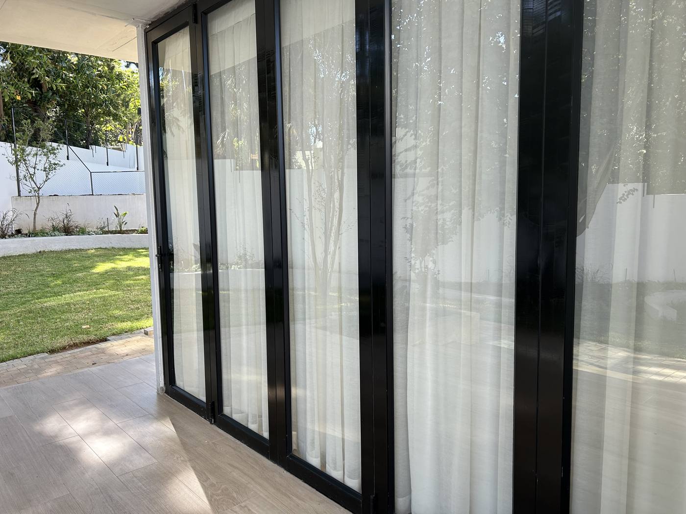 Black aluminium folding doors closed, sheer curtains behind the glass