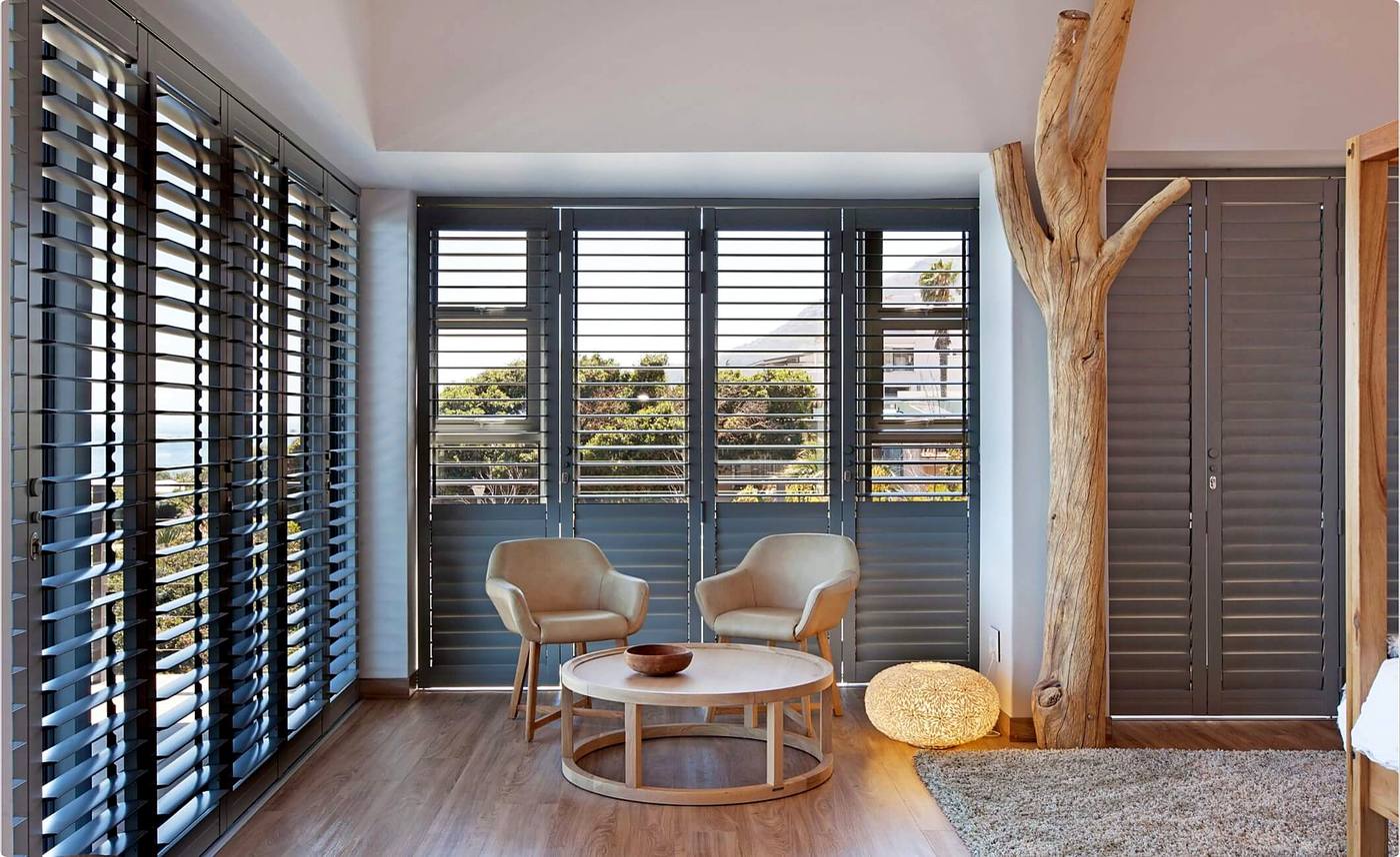 Charcoal shutters across two walls of a lounge, louvres open to the sea