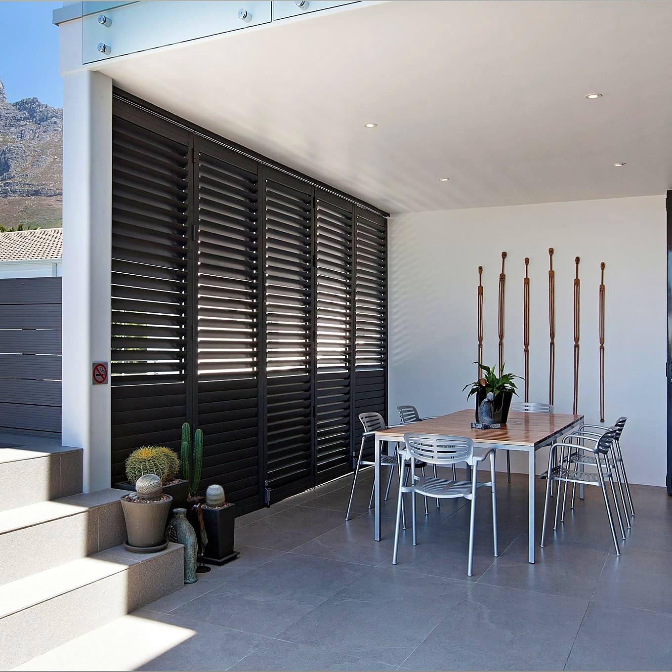 Charcoal aluminium shutters enclosing a covered patio below a Cape Town mountain ridge