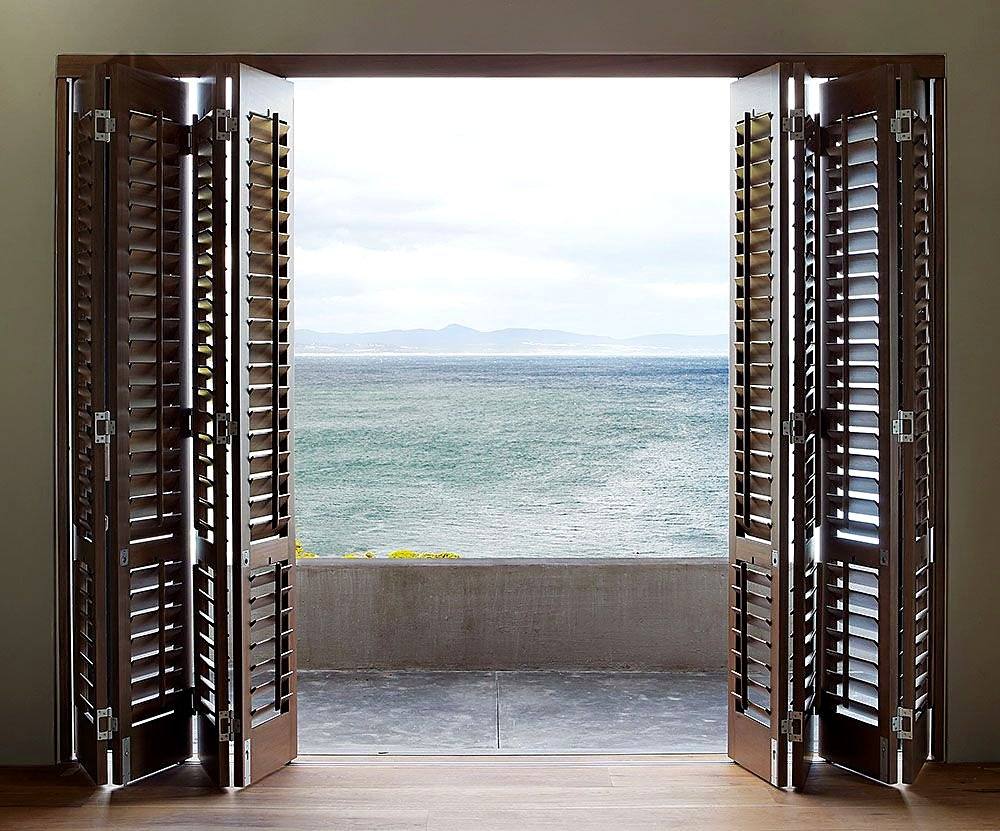 Dark timber-finish bi-fold shutters folded back to a balcony over the bay