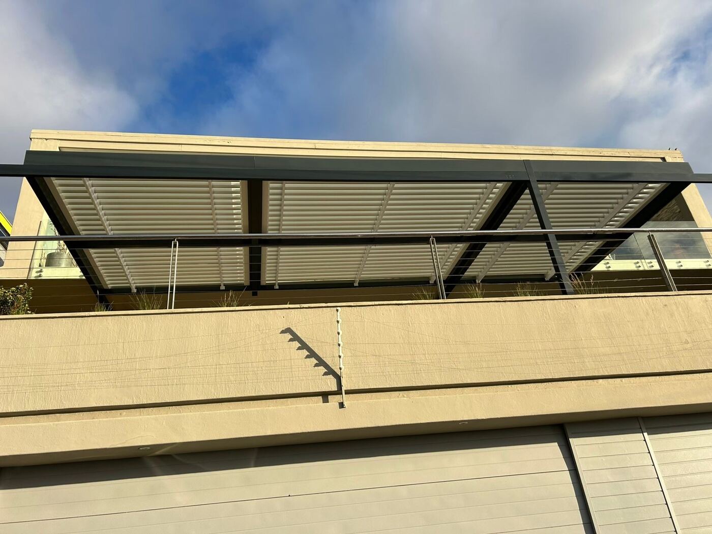 Charcoal frame, white blades aluminium louvre roof over a patio in Sea Point, Cape Town.