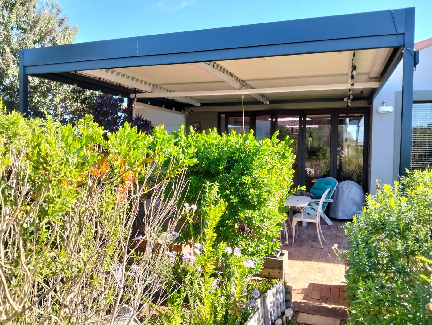 Cream drop awning on the corner of a charcoal louvre awning over a garden patio