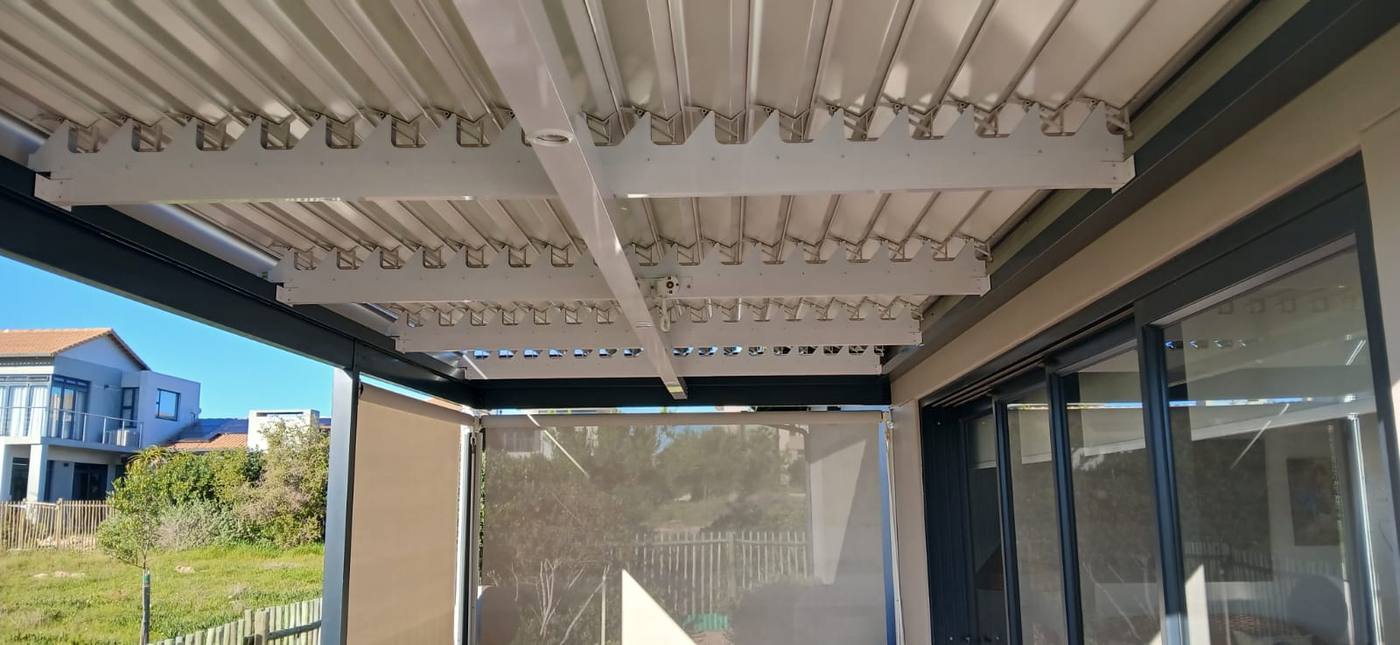 Two drop awnings part lowered in their guides under a louvre roof