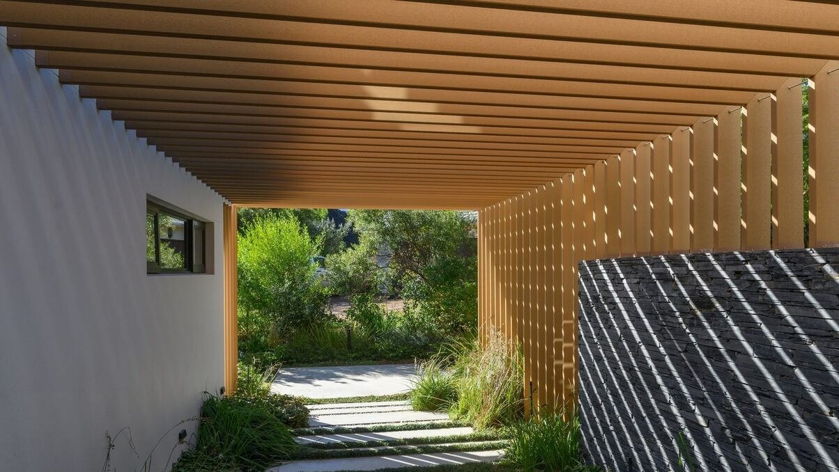 Timber-look composite slat pergola built by Aluminium Awnings over a garden walkway beside a slate-clad wall, Cape Town
