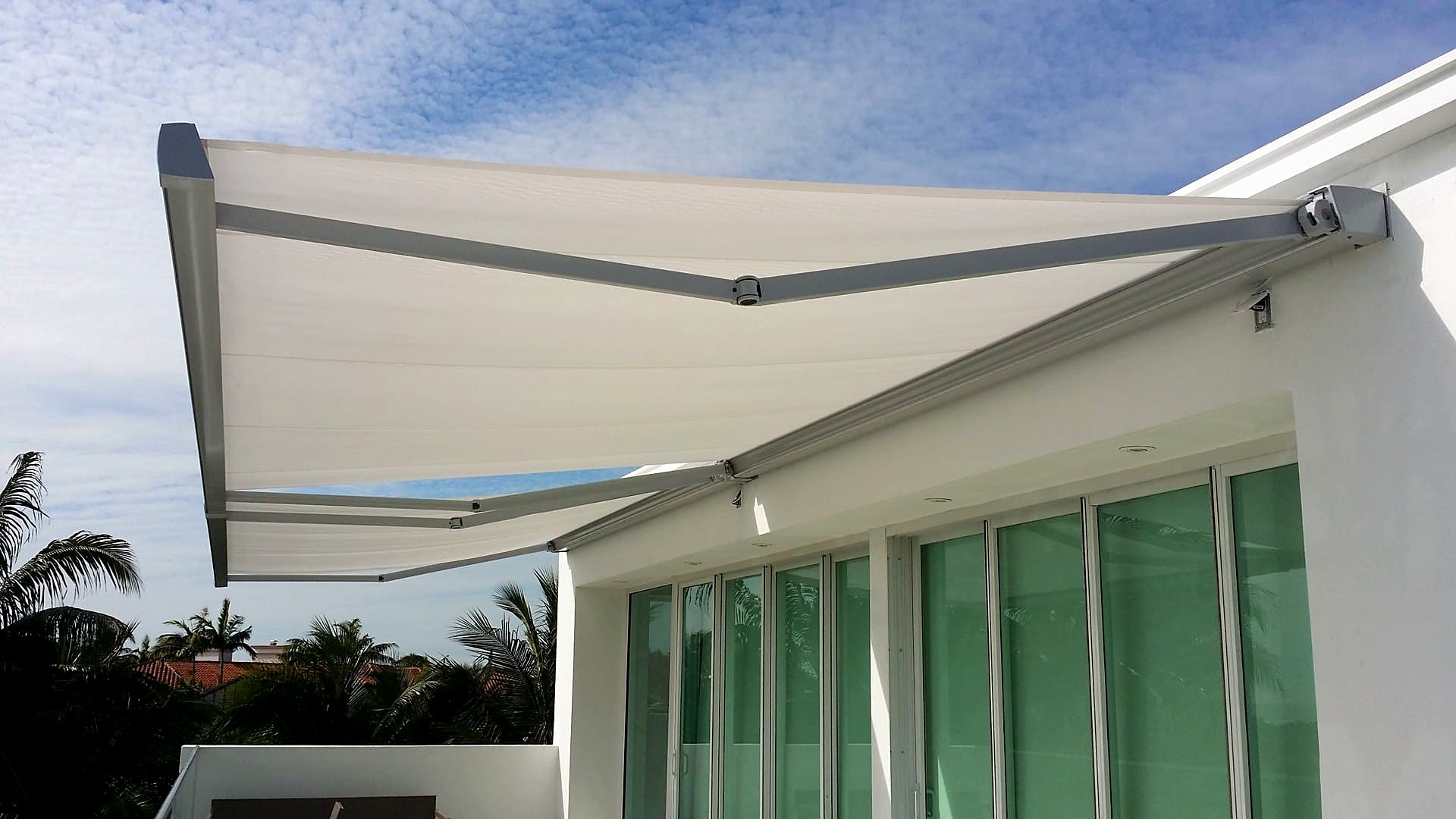 A pair of cream folding-arm awnings extended over sliding doors